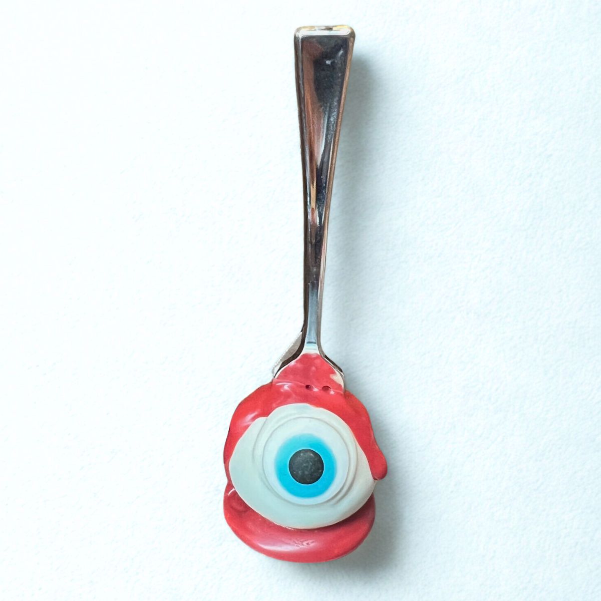 Spoon with a red eye-shaped handle on a white background
