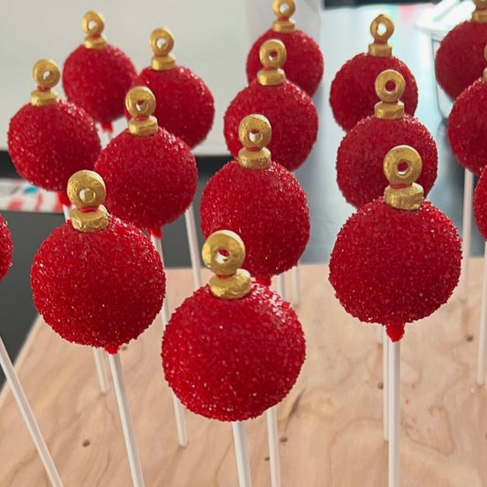 Red spherical treats on sticks with gold decorative elements on a blurred background