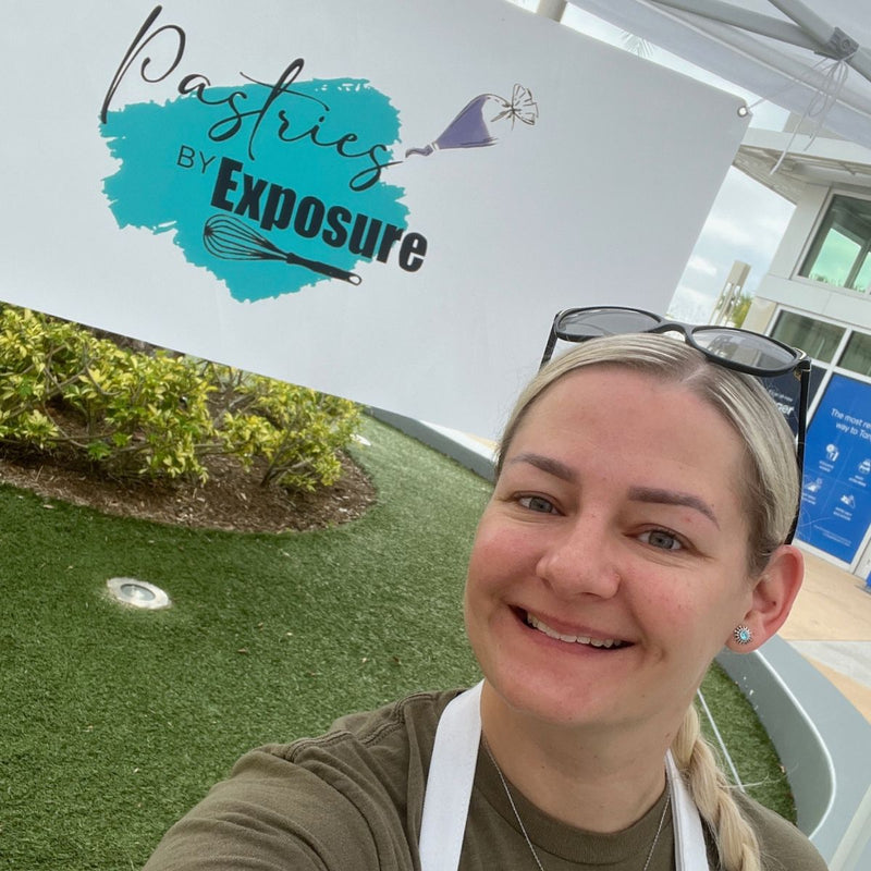 Woman in front of 'Pastries by Exposure' sign with greenery and building in the background