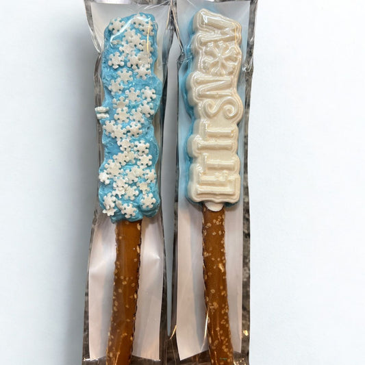 Two pretzel rods with decorative icing, one blue with white snowflake patterns and the other white with 'Merry Christmas' text, on a white background.
