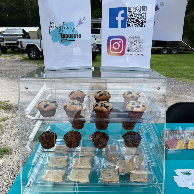 Three-tiered display of pastries with branded signs and social media icons on a teal table outdoors.