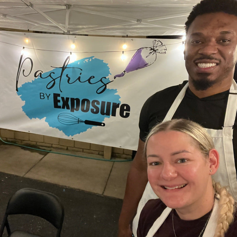 Two people wearing aprons standing in front of a 'Pastries by Exposure' sign.