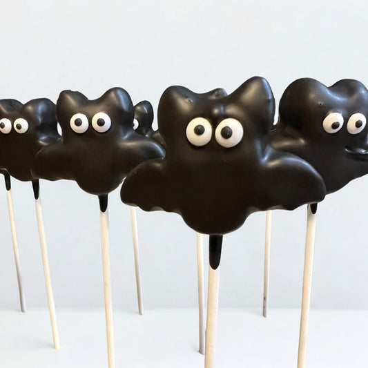 Black cloud-shaped treats on sticks with googly eyes against a white background