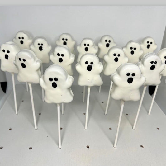 Ghost-shaped lollipops on sticks arranged on a white surface.