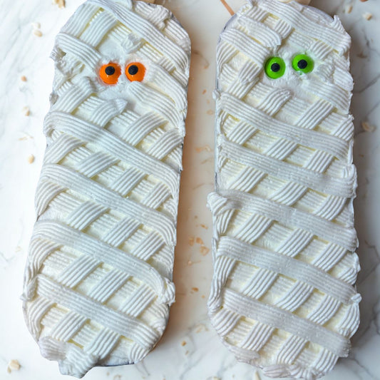 Two mummy-shaped cakes with candy eyes on a white surface